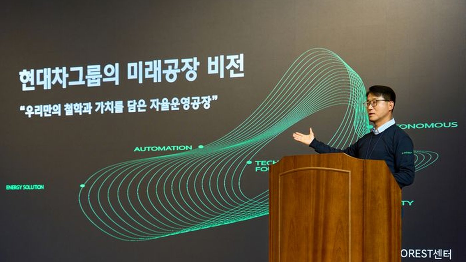 Choi Young-tae, head of the E-FOREST Center at Hyundai and Kia, gives a keynote at a podium in front of a screen showing the group's future factory vision